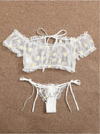 Conjunto Luiza frente, branco. Blusa cropped ciganinha e calcinha fio dental em renda transparente com margaridas, babados e laços.