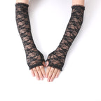Luva Valeria preta, par de luvas de renda fingerless com padrão floral elegante e babados, em mãos femininas. Vista frontal.