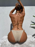 Mulher de costas com Biquíni Ondine bege de tela vazada. Top triângulo halter neck e calcinha de amarrar com argolas laterais.