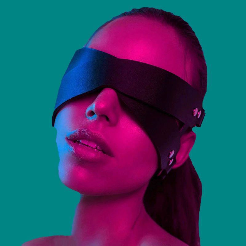 Máscara Minuit preta em couro premium. Venda para olhos, com tiras laterais e fivelas. Detalhe frontal vestida em mulher. NuAuge.