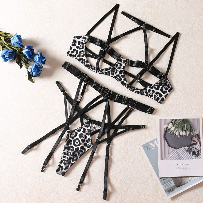 Conjunto Leopoldina: sutiã com bojo e tiras strappy, calcinha fio dental e cinta liga, todos com estampa leopardo e detalhes pretos.