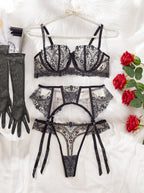 Conjunto Vivienne preto de frente. Sutiã de aro, bordado em renda preta e mesh transparente. Cinta liga e tanga combinando.