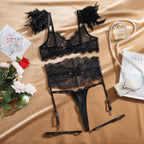 Conjunto Nyx preto, vista frontal. Sutiã de renda transparente com aro, detalhes de penas, cinta-liga e calcinha fio dental.
